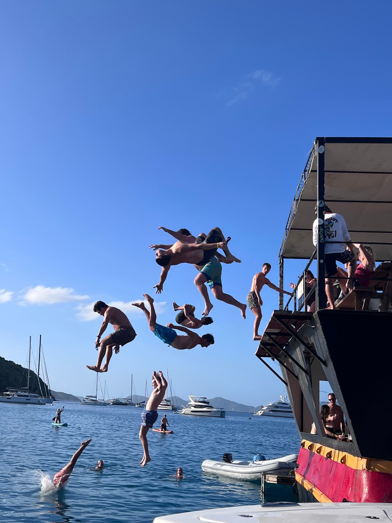 Seven friends mid-air, jumping off the top deck of the Willy T at Norman Island